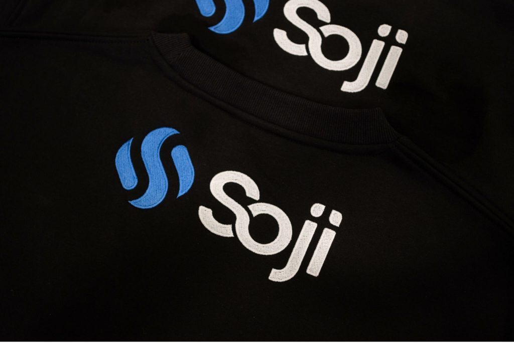 A stack of sweaters with the Soji logo on the top back.