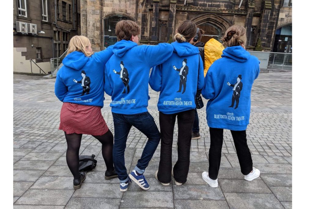 Line of four Bluetooth Kevin Theatre members showing off the backs of their hoodies.