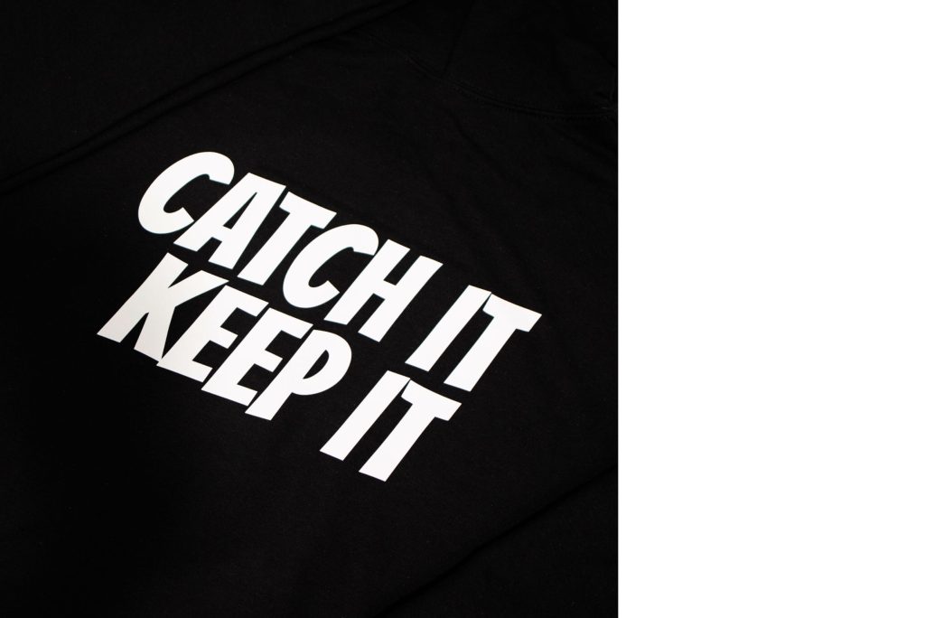 Logo that reads 'CATCH IT KEEP IT' on the back of a folded hoodie.